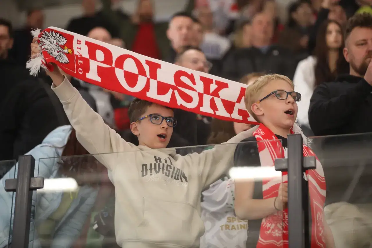 Dwóch chłopców kibicuje, trzymając biało-czerwoną flagę z napisem