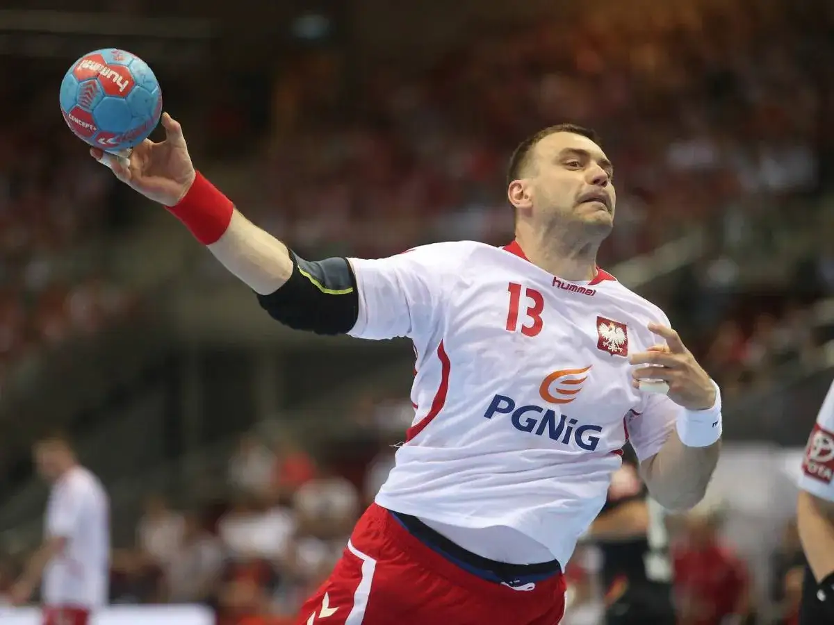 Bartosz Szczepanik w akcji, rzuca piłką do bramki. Zawodnik w białej koszulce z numerem 13 i godłem Polski.