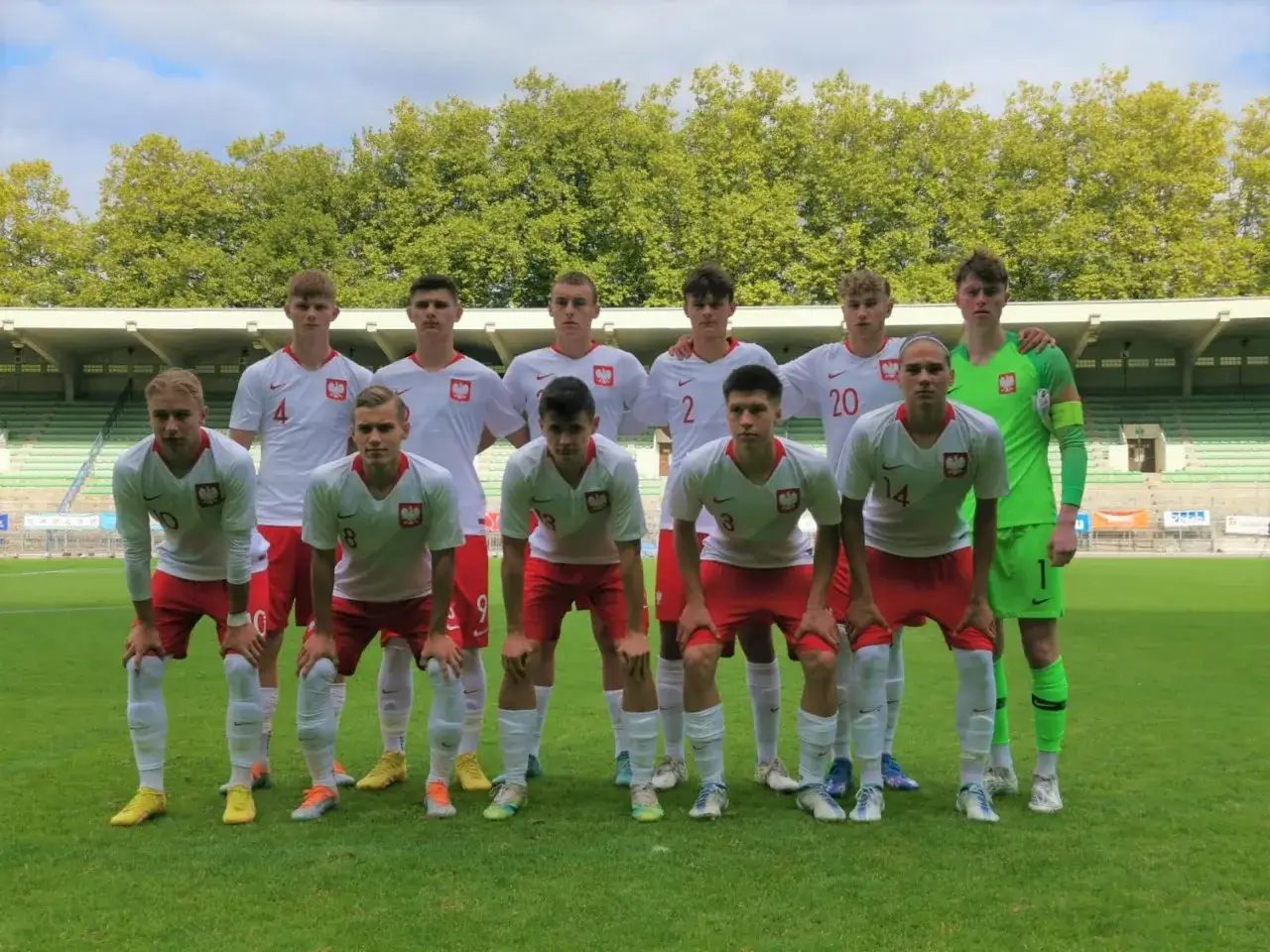 Drużyna Polski U17 na Mistrzostwach Europy. Młodzi piłkarze w białych koszulkach i czerwonych spodenkach pozują na boisku.