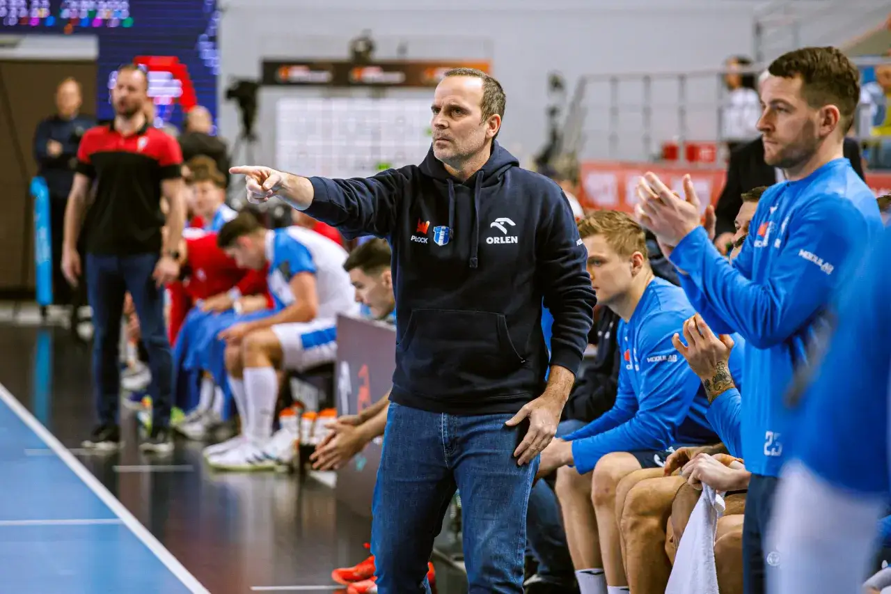 Trener Wisły Płock PSG wskazuje palcem, udzielając wskazówek zawodnikom siedzącym na ławce.