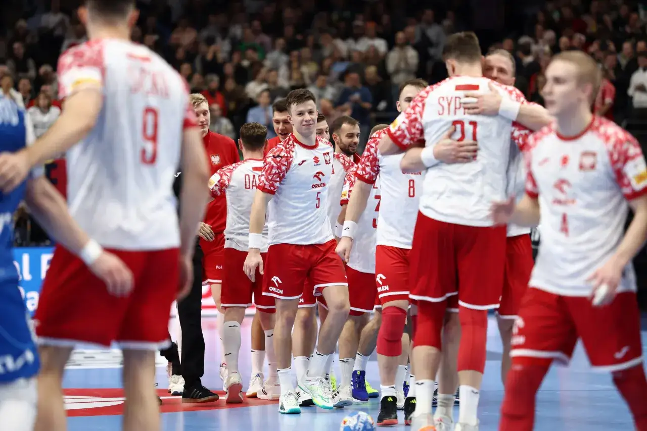 Drużyna Polski w piłce ręcznej świętuje zwycięstwo nad Serbią. Zawodnicy w biało-czerwonych strojach cieszą się na boisku.