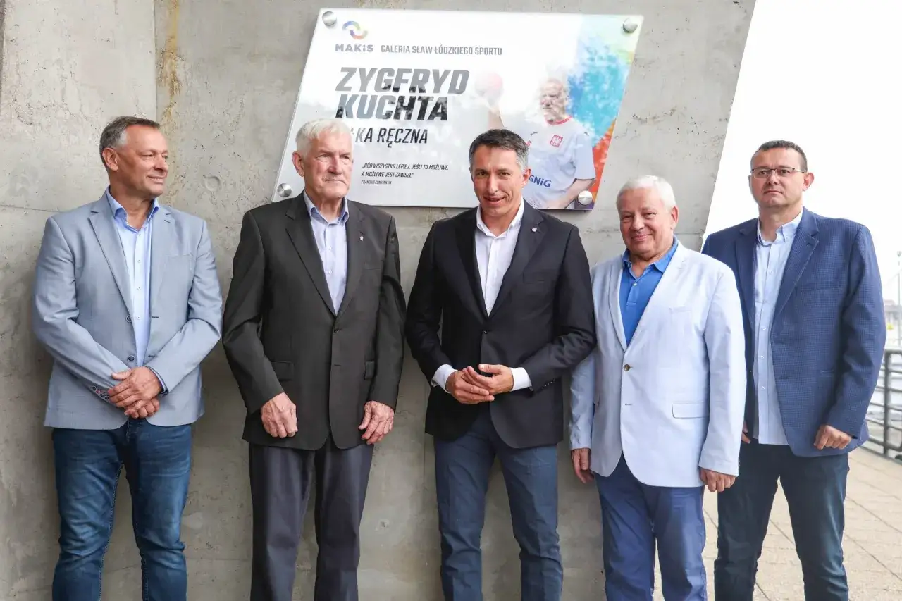 Pięciu mężczyzn pozuje przed tablicą upamiętniającą Zygfryda Kuchta, legendę piłki ręcznej.