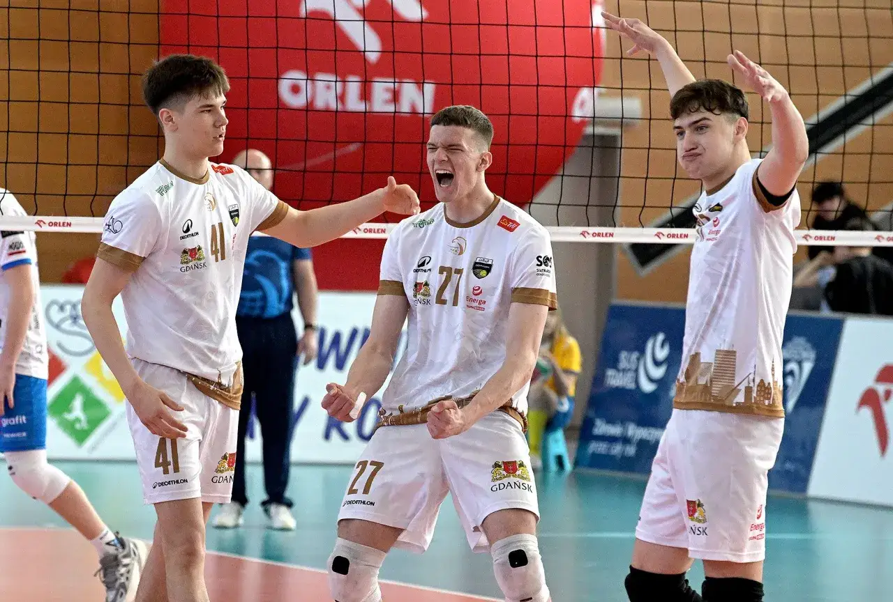 Trzech młodych siatkarzy w białych strojach świętuje zwycięstwo na mistrzostwach polski junior&oacute;w.