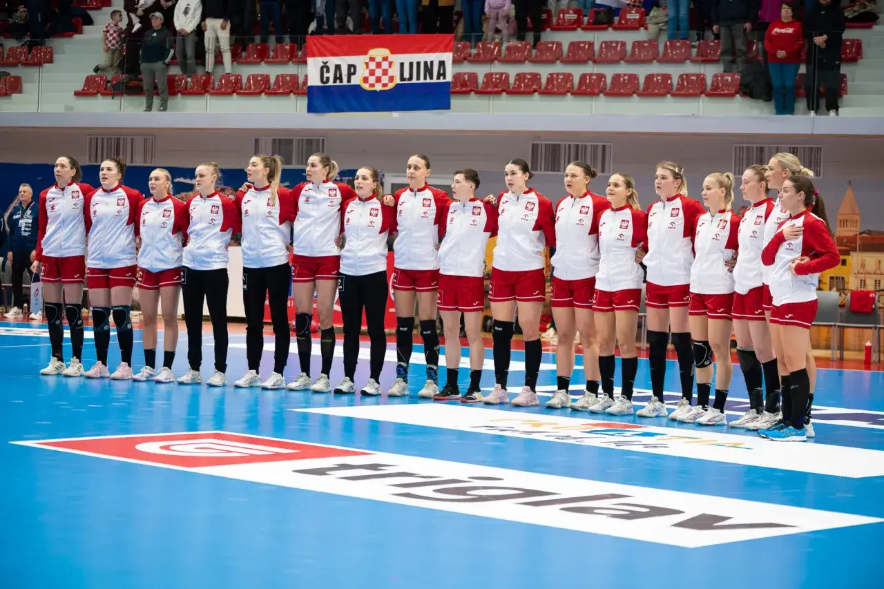 Drużyna Polski na Mistrzostwach Świata w piłce ręcznej kobiet. Zawodniczki w strojach z orłem na piersiach stoją na niebieskiej hali.