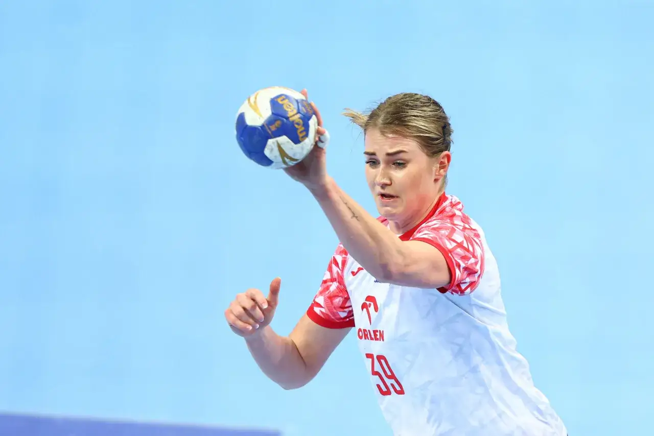 Natalia Nosek, zawodniczka z numerem 39, w białej koszulce z czerwonymi wzorami, rzuca piłkę do ręcznej.