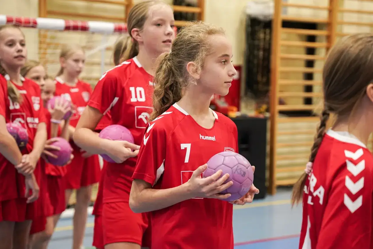 Młode szczypiornistki KS Bystra w czerwonych strojach z piłkami.