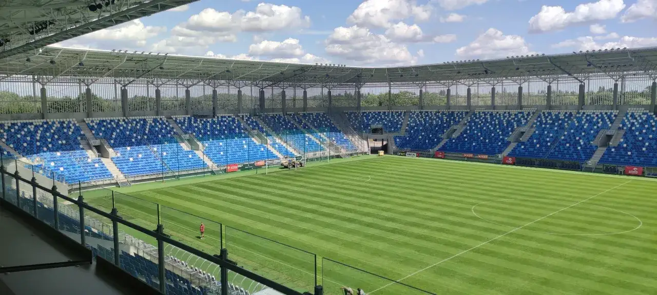 Pusta trybuna stadionu w Płocku, gotowa na kolejny mecz. Pięknie przystrzyżona murawa czeka na piłkarzy.