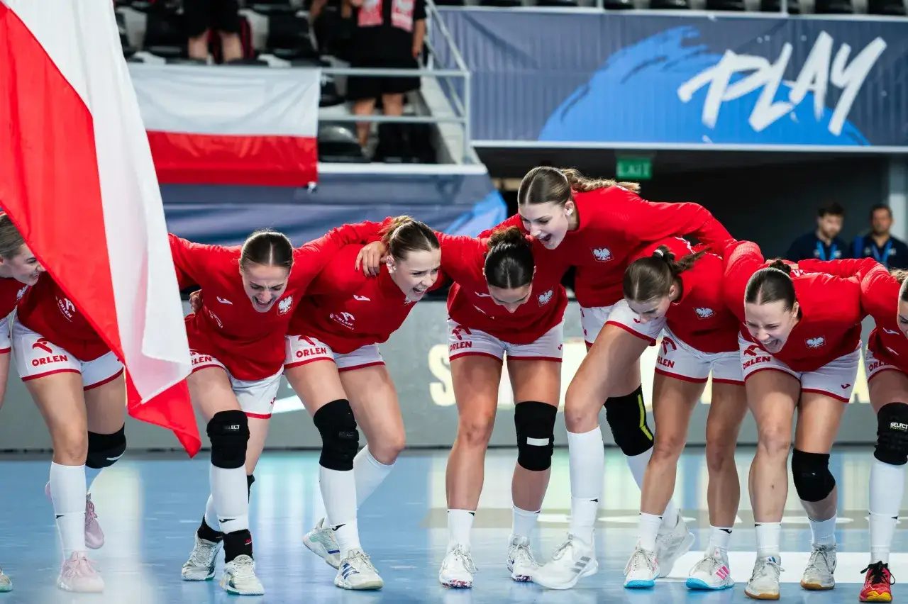 Drużyna piłki ręcznej w biało-czerwonych strojach, z flagą Polski, świętuje sukces w pierwszej lidze piłki ręcznej.