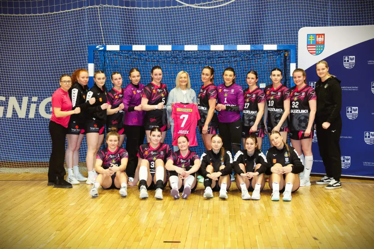 Drużyna Suzuki Korona Handball Kielce pozuje do zdjęcia. W centrum kobieta trzyma koszulkę z numerem 7.