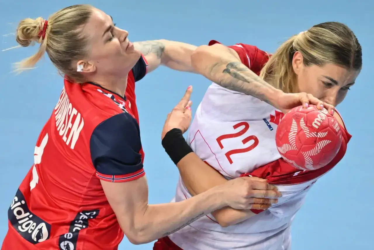 Zacięta walka o piłkę w meczu piłki ręcznej. Zawodniczka z Norwegii w czerwonej koszulce pr&oacute;buje odebrać piłkę rywalce.
