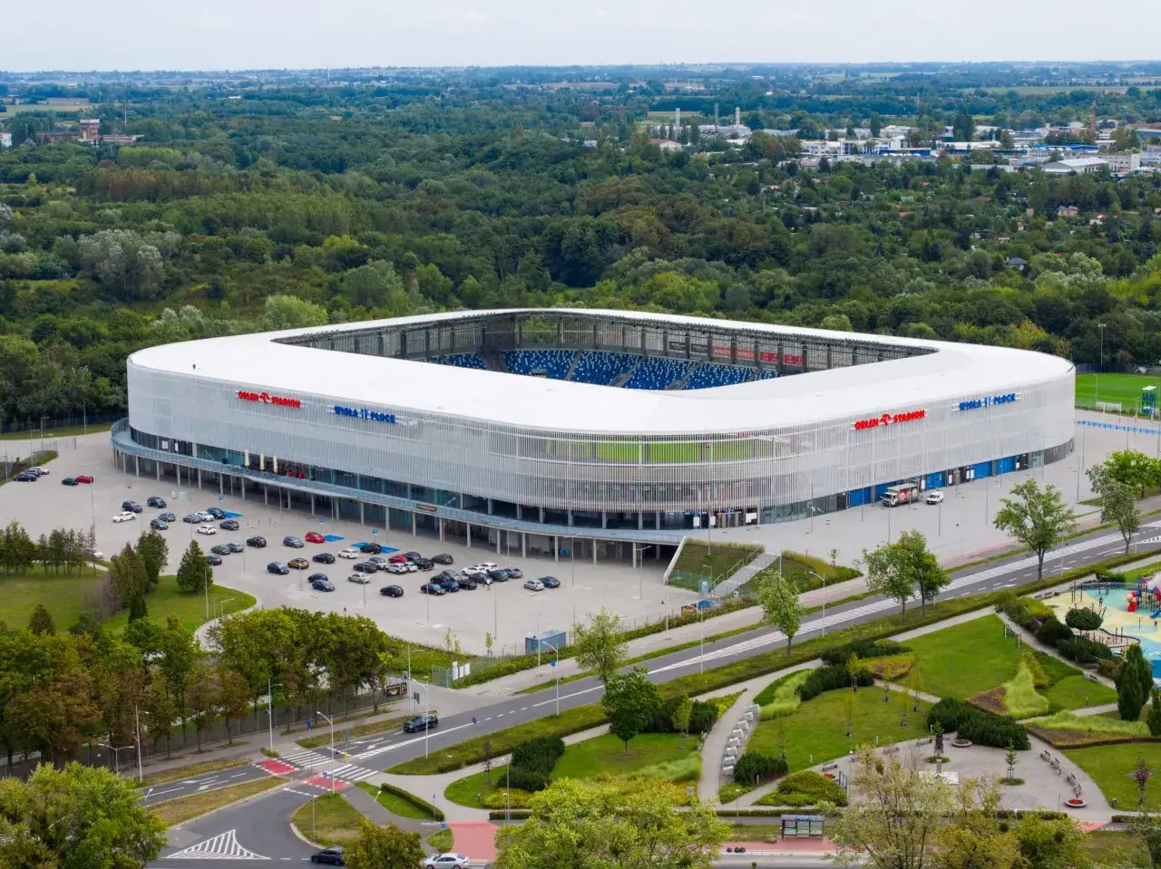 Nowoczesny stadion Wisły Płock z niebieskimi trybunami, otoczony zielenią i parkingiem. Idealne miejsce na emocjonujący mecz Płock.