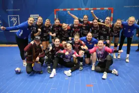 Drużyna piłki ręcznej KPR Bukowsko Dopiewo świętuje zwycięstwo. Radosne zawodniczki w strojach sportowych, z numerami na koszulkach, pozują do zdjęcia z trenerem.