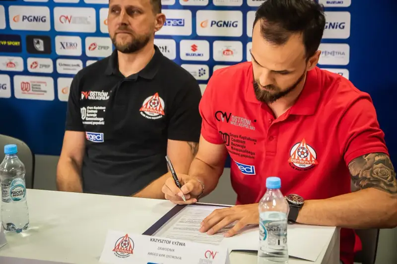 Krzysztof Łyżwa, zawodnik ARGED KPR Ostrovia, podpisuje dokumenty. Obok siedzi trener.